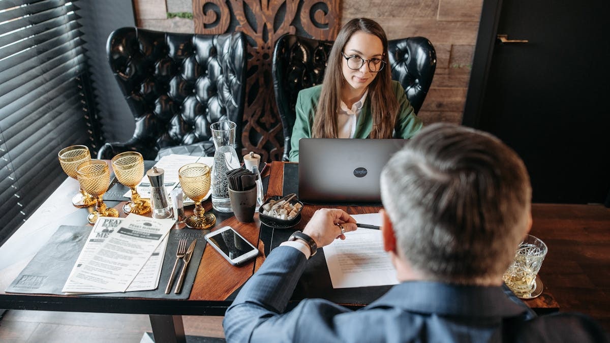 A professional business meeting indoors with two adults discussing and working on laptops.