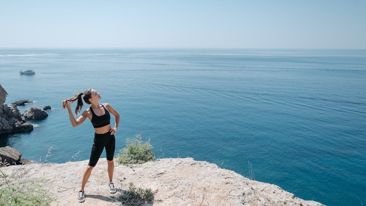 Woman on cliff overlooking ocean, embodying fitness and wellness in activewear.